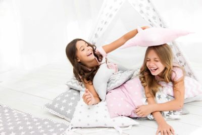 two girls playful pillow fight in teepee with pink pillows